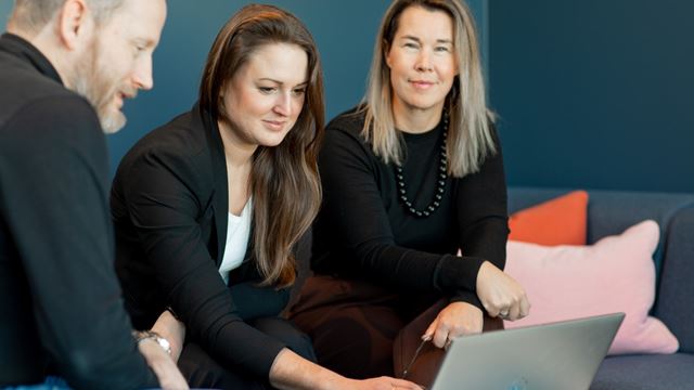 tre Wihlborgskollegor kollar på en dator tillsammans i ett mötesrum