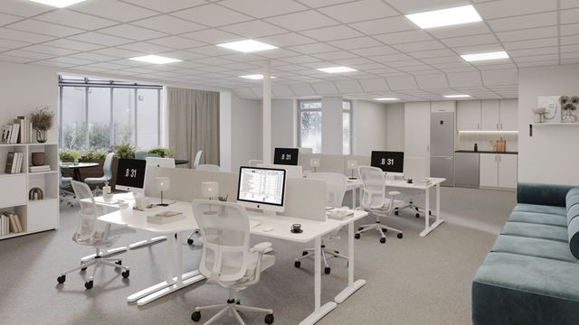 Ljust kontor med konstorsbord, datorer och en mörkgrön soffa