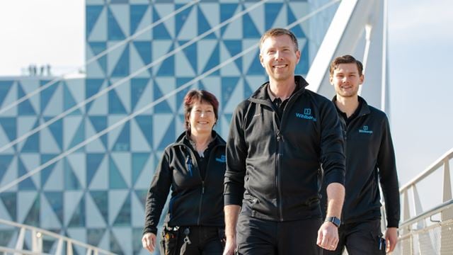 Fastighetsvärdar går över en bro i Helsingborg, med fastigheten Prisma i bakgrunden