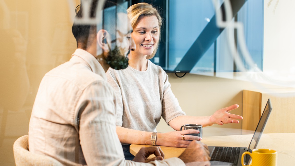 Två kollegor arbetar framför en dator i ett mötesrum. 