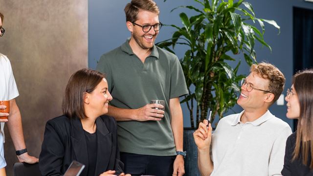 Tre kollegor sitter ner och en står bredvid och pratar med de andra.