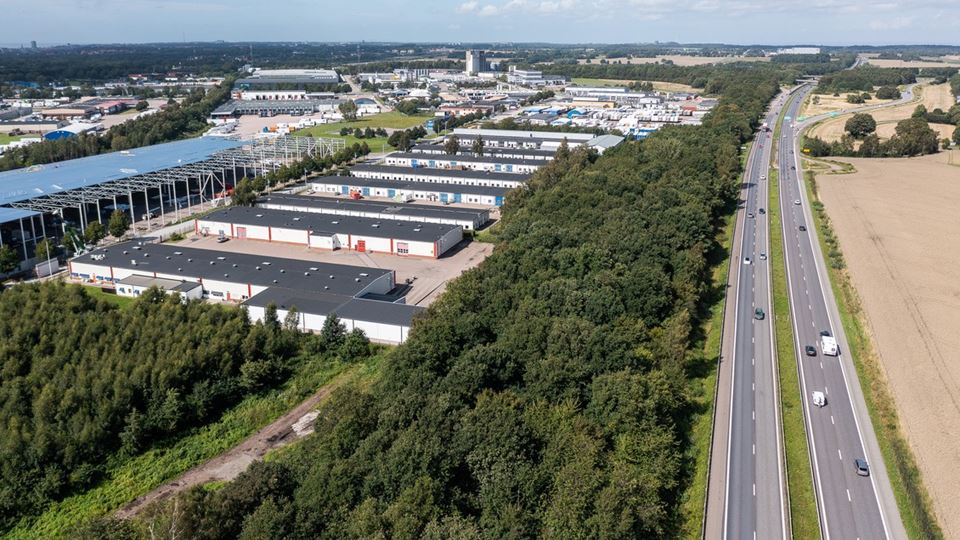 Bild tagen ovanirfrån på ett av husen i längorna i närområdet för den tomma tomten. Höstig miljö och vitt hus emd svart tak. Man ser även asfalt och parkeringsmöjligheter bredvid