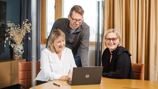 Glada medarbetare som samlas runt en dator.