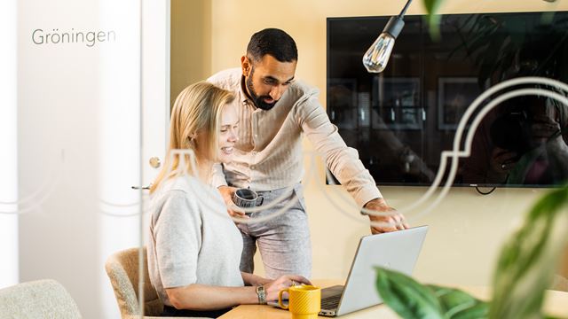 Två personer sitter runt ett bord och tittar på en dator.