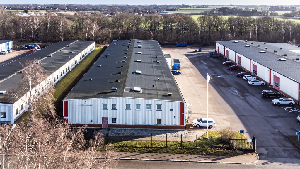 Bild tagen ovanirfrån på ett av husen i längorna i närområdet för den tomma tomten. Höstig miljö och vitt hus emd svart tak. Man ser även asfalt och parkeringsmöjligheter bredvid