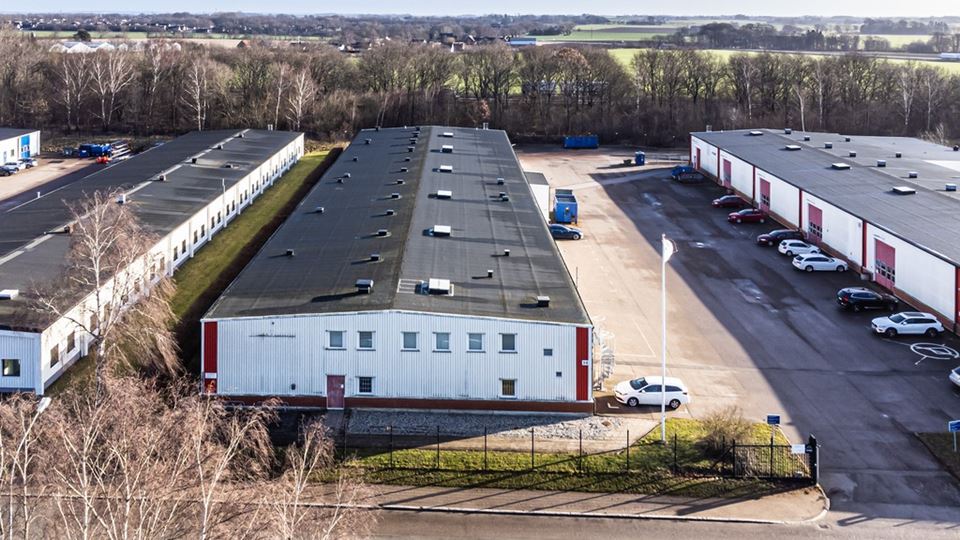 Bild tagen ovanirfrån på ett av husen i längorna i närområdet för den tomma tomten. Höstig miljö och vitt hus emd svart tak. Man ser även asfalt och parkeringsmöjligheter bredvid