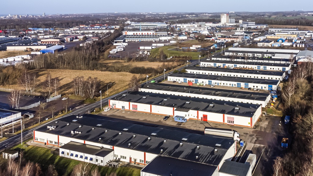 Bilden är tagen ovanifrån och visar längor av hus i en höstig miljö. Vita hus med svarta tak