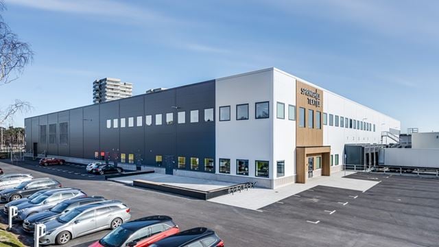 Bild tagen en solig dag med blå himmel. Visar byggnaden med vit och grå fasad, samt parkeringsmöjligheter för både cykel och bil utanför. Spring Hills logga över ingången och ett höghus i bakgrunden