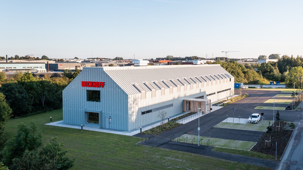 Vit kontorsbyggnad i två plan med träd och grönska i förgrunden.