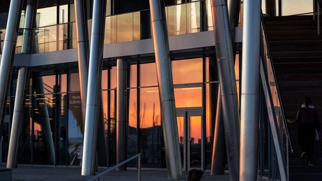 Bilden visar fasaden som bestå av fönster och pelare. I fönstret speglas solnedgången