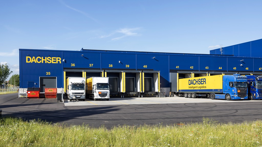 Bilden visar den blåa byggnaden med gula detaljer. Lastportar och lastbilar