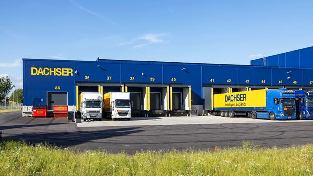 Bilden visar den blåa byggnaden med gula detaljer. Lastportar och lastbilar