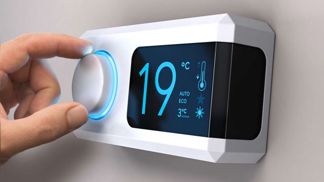 En hand som vrider på en termostat i en byggnad.