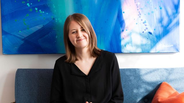 Malin sitter i en blå soffa framför en blå tavla.