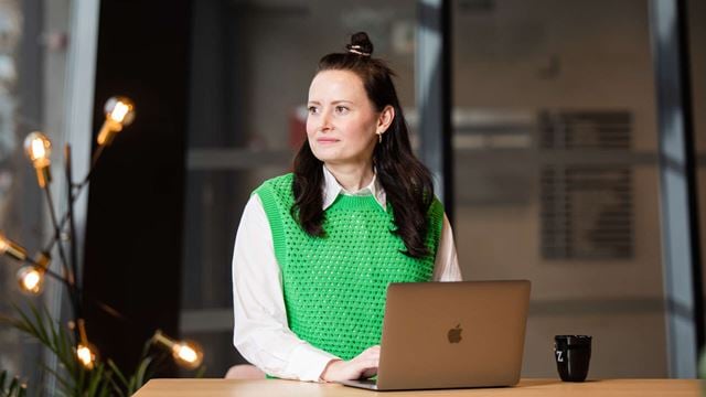 Mörkhårig kvinna i grön tröja sitter framför en dator.