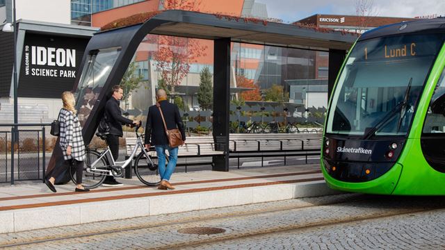 Tre personer som går mot Lunds spårvagn vid en hållplats.