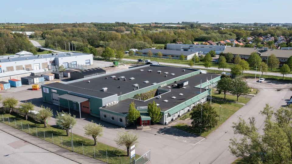 Flygfoto av en lager- och kontorslokal med gröna detaljer, staket runt hela fastigheten, Vårbuketten 2 i Malmö.