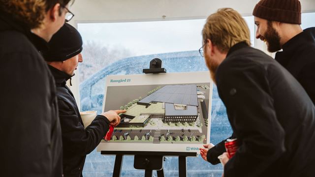 Fyra personer tittar på ett staffli där en illustration av den färdiga byggnaden på Rausgård 21 visas.