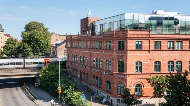 Tegelfastigheten Armaturen med takterass överst. Ett tåg passerar över en vägtunnel i bakgrunden.